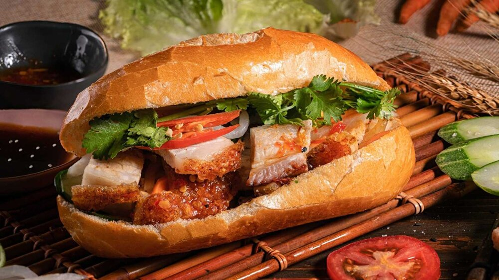 Một ổ bánh mì Việt Nam nóng hổi, vàng ươm, thơm lừng mùi bơ pate, nhân đầy ắp rau dưa và thịt tươi ngon, là món ăn lý tưởng cho bữa sáng hoặc bữa trưa hấp dẫn.
